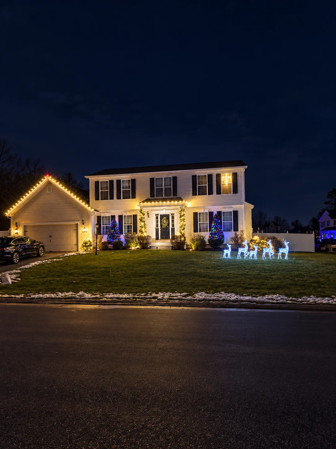 Home with warm white holiday lights and illuminated reindeer on the front lawn