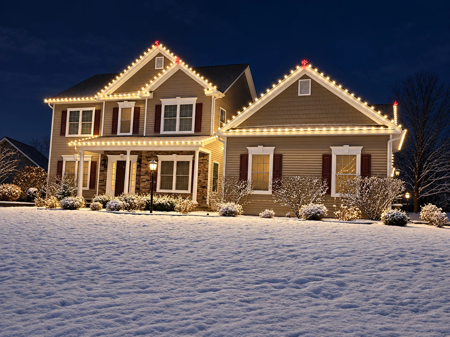 Two-story home with warm white roofline lights above a snow-covered front yard